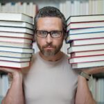 Portret nauczyciela w klasie bibliotecznej Nauczyciele w bibliotece uniwersyteckiej Dzień Nauczycieli Zabawny nauczyciel trzyma wiele książek Szalony nauczyciel z książkami Podekscytowany nauczyciel w szkolnej bibliotece książek