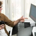 Twórca IT trzymający filiżankę kawy z oglądającym oprogramowanie online na komputerze Gusher