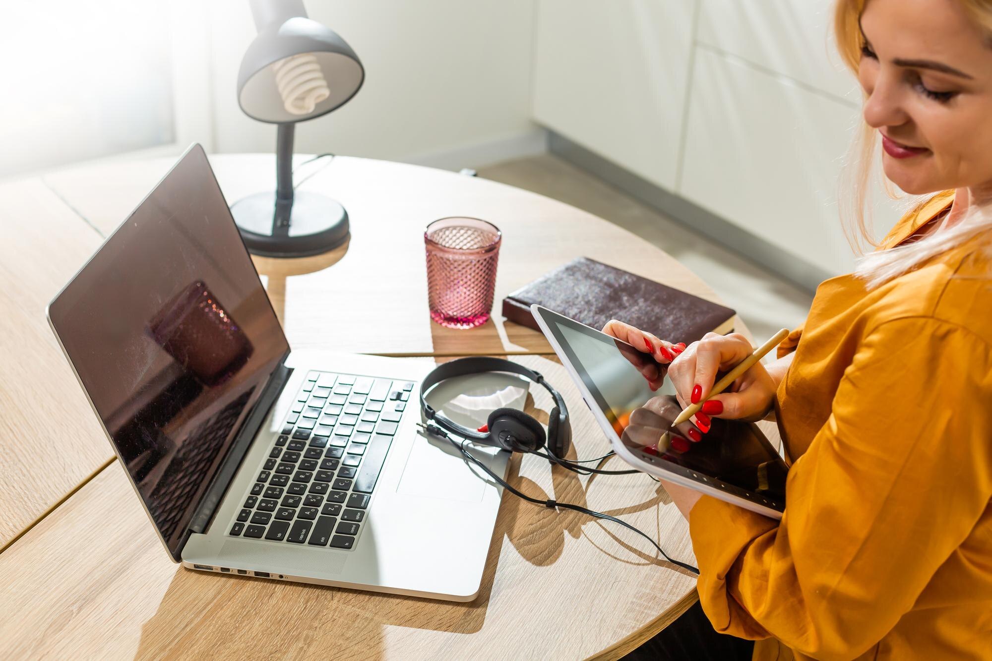 Młoda kobieta siedzi w kuchni i pracuje na laptopie.