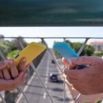 Kilka osób trzyma telefon komórkowy w pokrowcach dopasowanych do ubrania Stojąc na moście nad ruchem miejskim