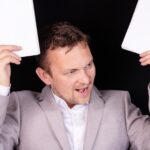 Sfrustrowany i zirytowany biznesmen z gniewnymi emocjami na twarzy i papierami w rękach. Pomysł na biznes.